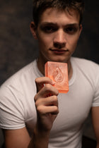 Man holding a bar of soap with a drop design against a dark background