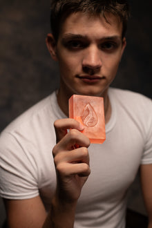 Man holding a bar of soap with a drop design against a dark background